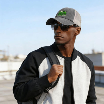 Man wearing a black and gray jacket, sunglasses, and a cap with text outdoors.